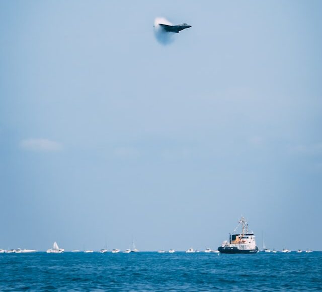 Picture of a supersonic jet flying over a ship on the sea. also visible is it breaking the sound barrier 