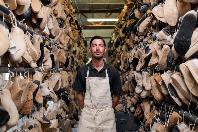 A man standing in between rows of half manufactured shoes in a workshop